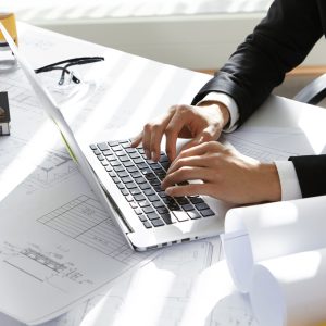 hands-ceo-construction-company-black-suit-typing-message-via-e-mail-partners-laptop-with-drawings-seal-stamp-divider-table-min